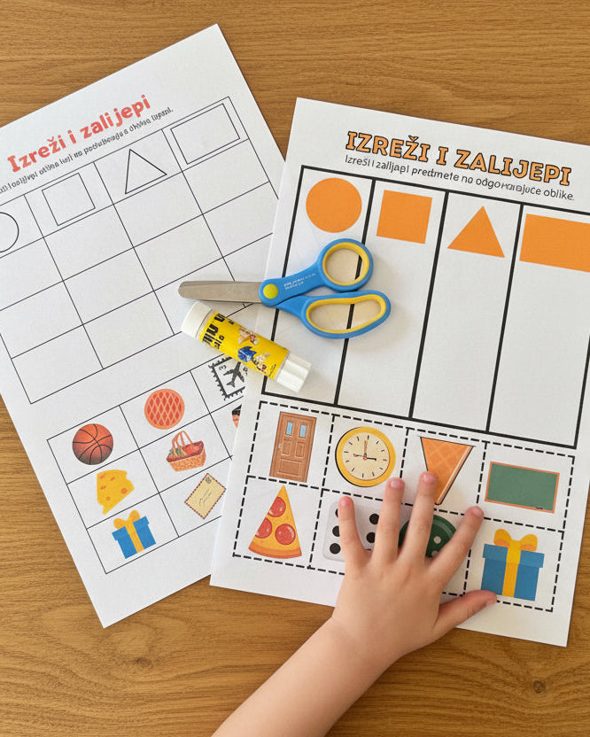 Child's hand with scissors on educational worksheets on a dark surface